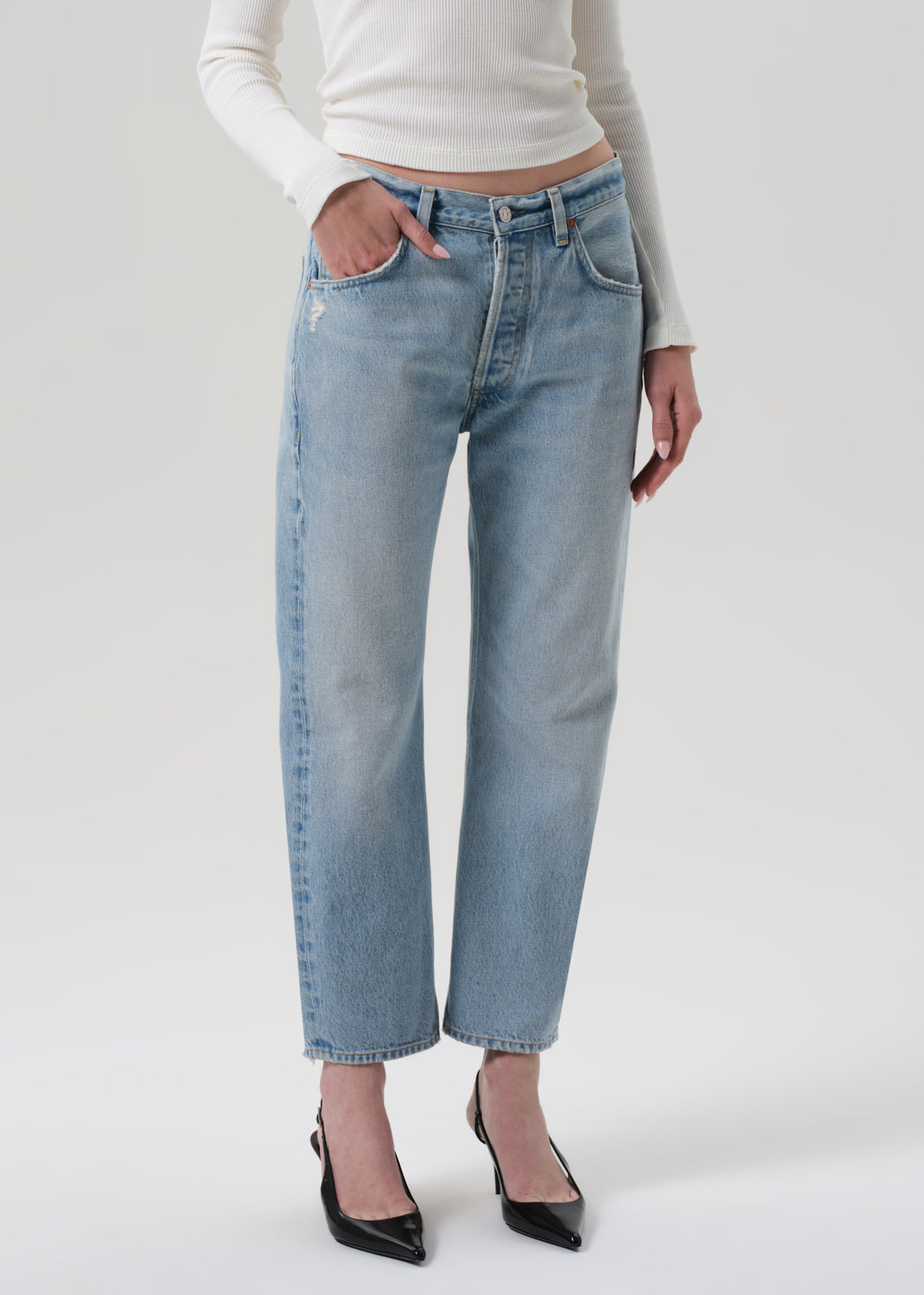 Person wearing light blue jeans and a white top on a plain background