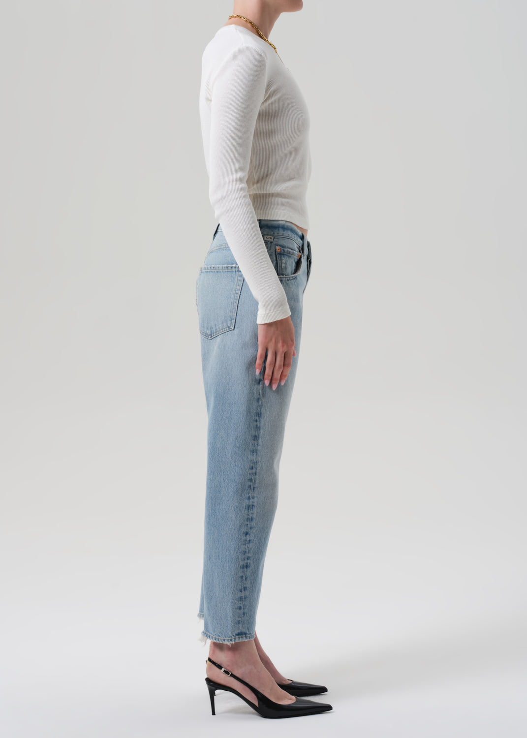 Person wearing light blue jeans and a white long-sleeve shirt on a plain background