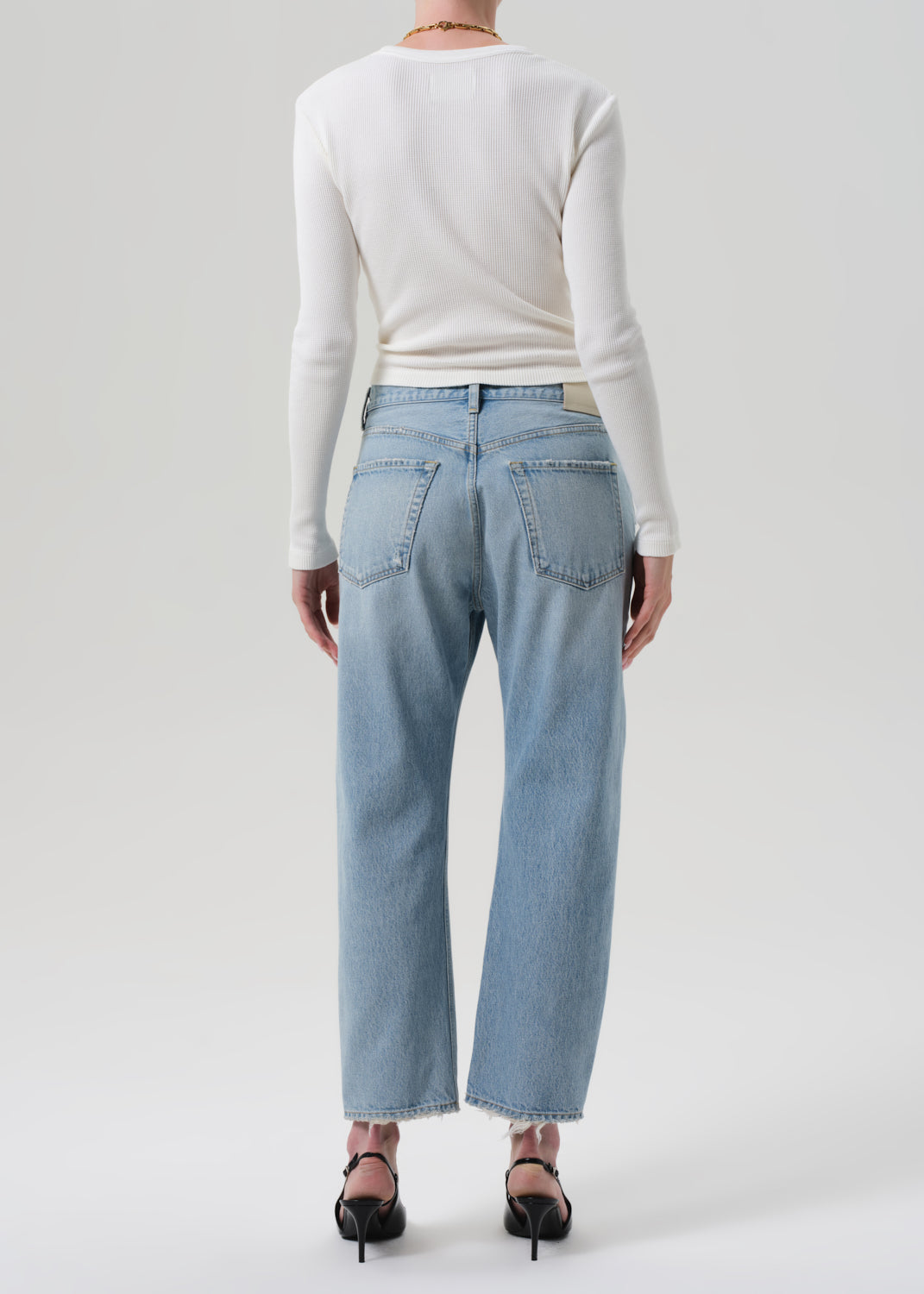 Person wearing light blue jeans and a white long-sleeve shirt on a plain background