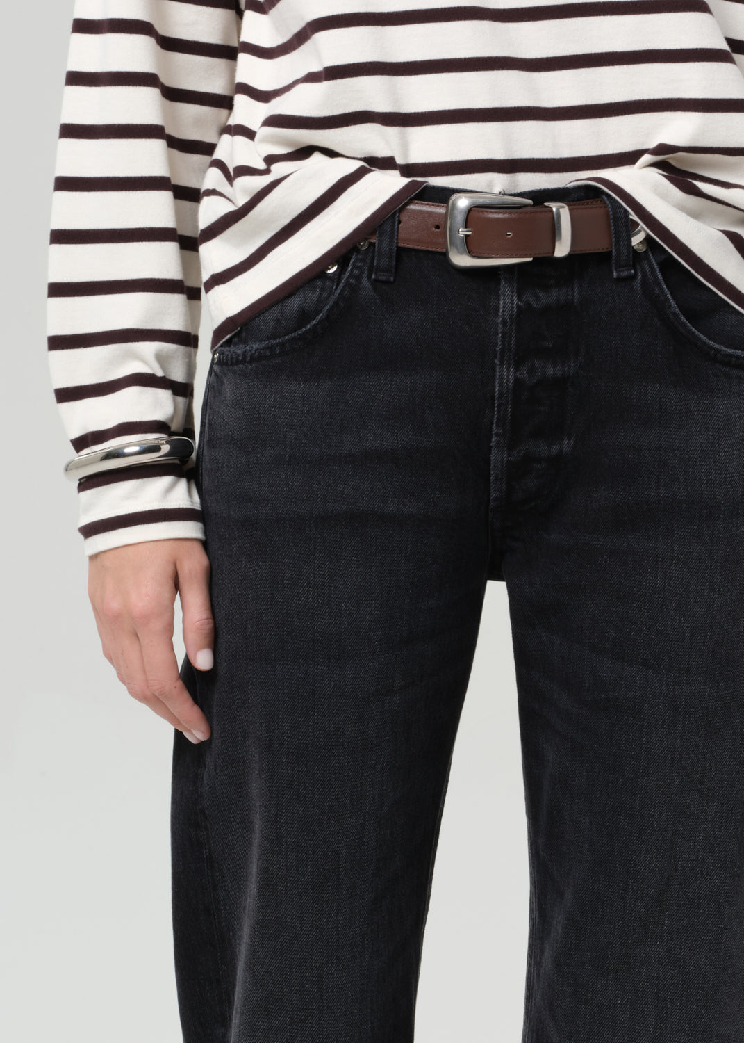 Person wearing a brown and white striped shirt and black jeans on a plain background