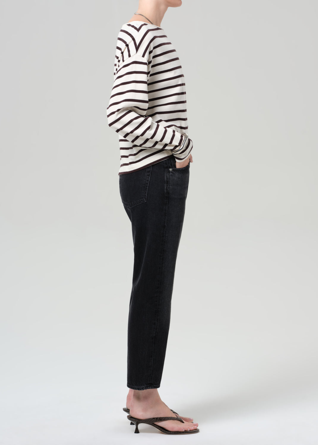 Person wearing a brown and white striped shirt and black jeans on a plain background