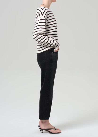 Person wearing a brown and white striped shirt and black jeans on a plain background