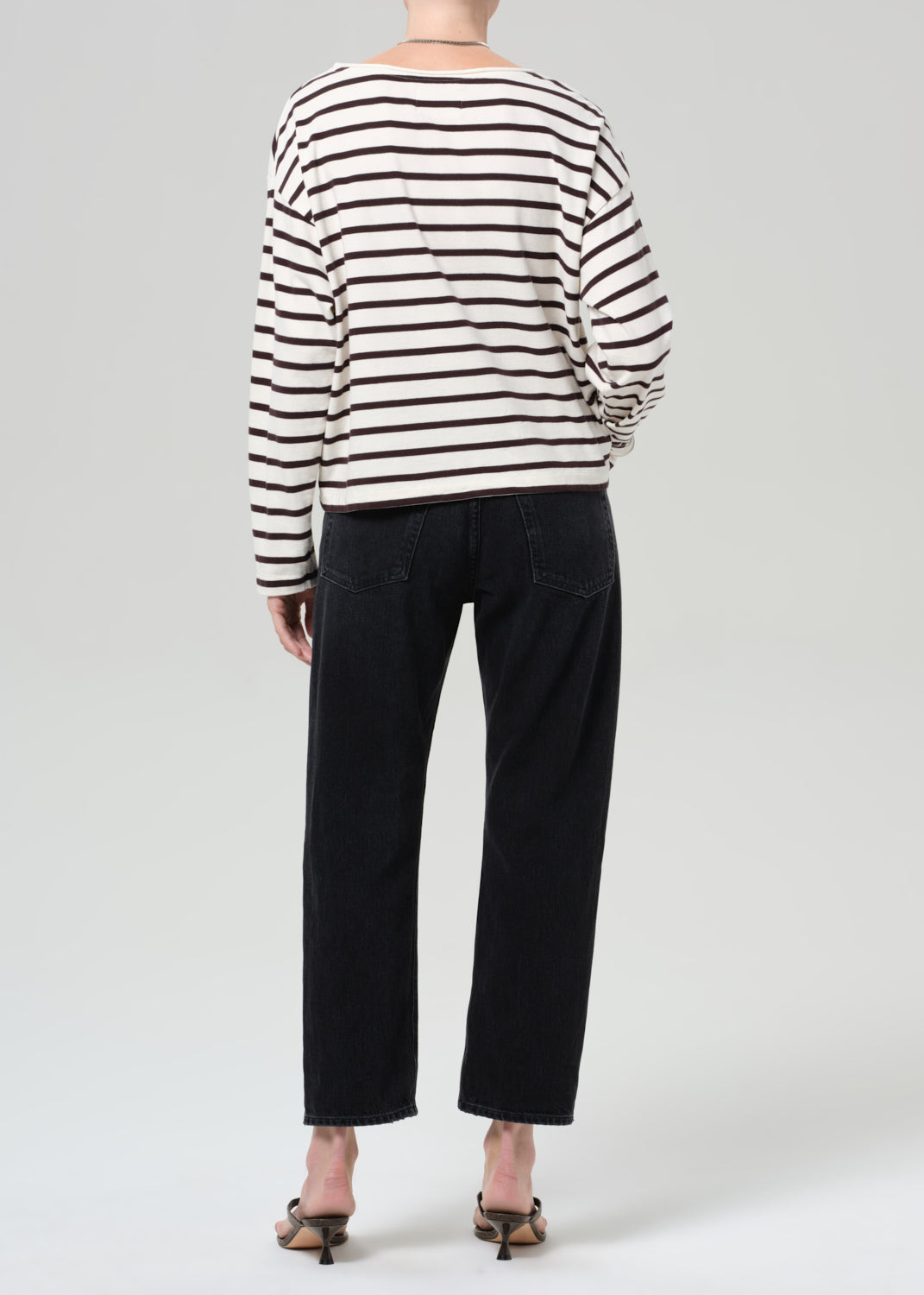 Person wearing a brown and white striped shirt and black jeans on a plain background