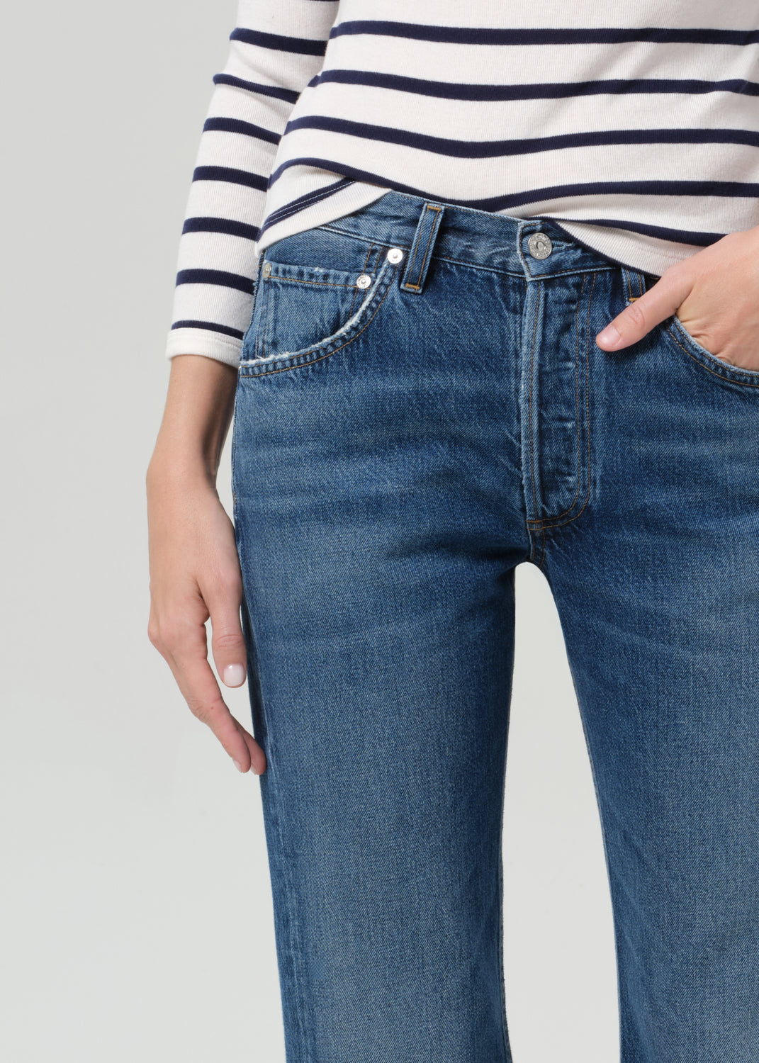 Person wearing a striped shirt and blue jeans on a grey background