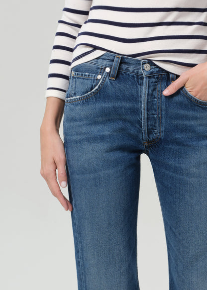 Person wearing a striped shirt and blue jeans on a grey background