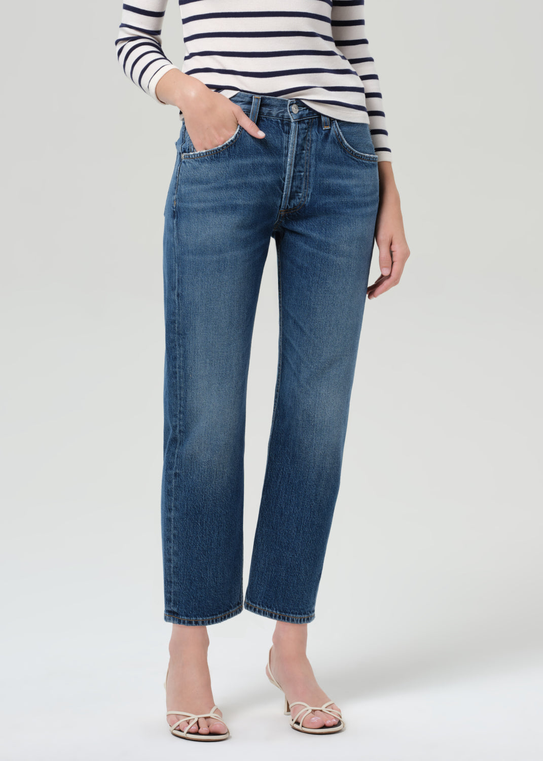 Person wearing a striped shirt and blue jeans on a grey background