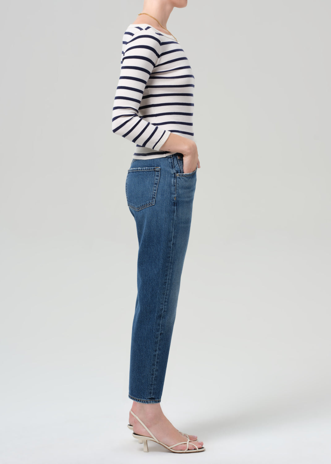 Person wearing a striped shirt and blue jeans on a grey background