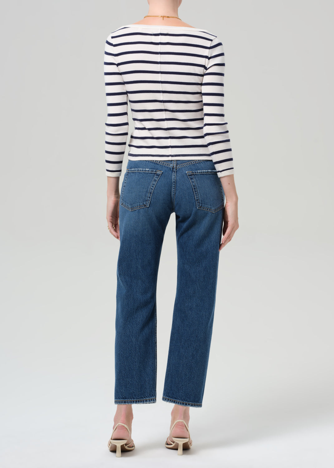 Person wearing a striped shirt and blue jeans on a grey background