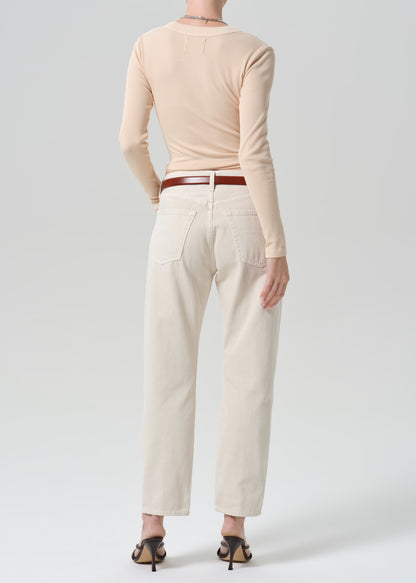 A model shown from the back wearing a light peach long-sleeve top, off-white straight-leg jeans with a brown leather belt, and black heeled sandals against a grey background.