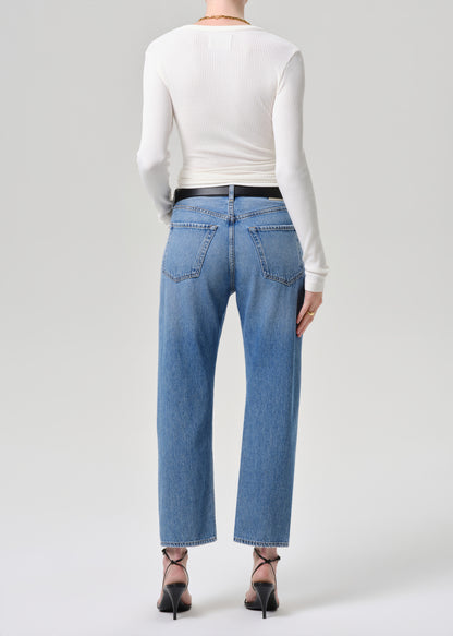 A model shown from the back wearing light-wash blue straight-leg jeans, a white long-sleeve top, and black high heels against a grey background.