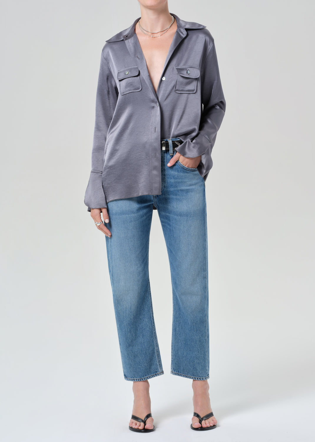 Person wearing a gray button-up shirt and blue jeans on a grey background