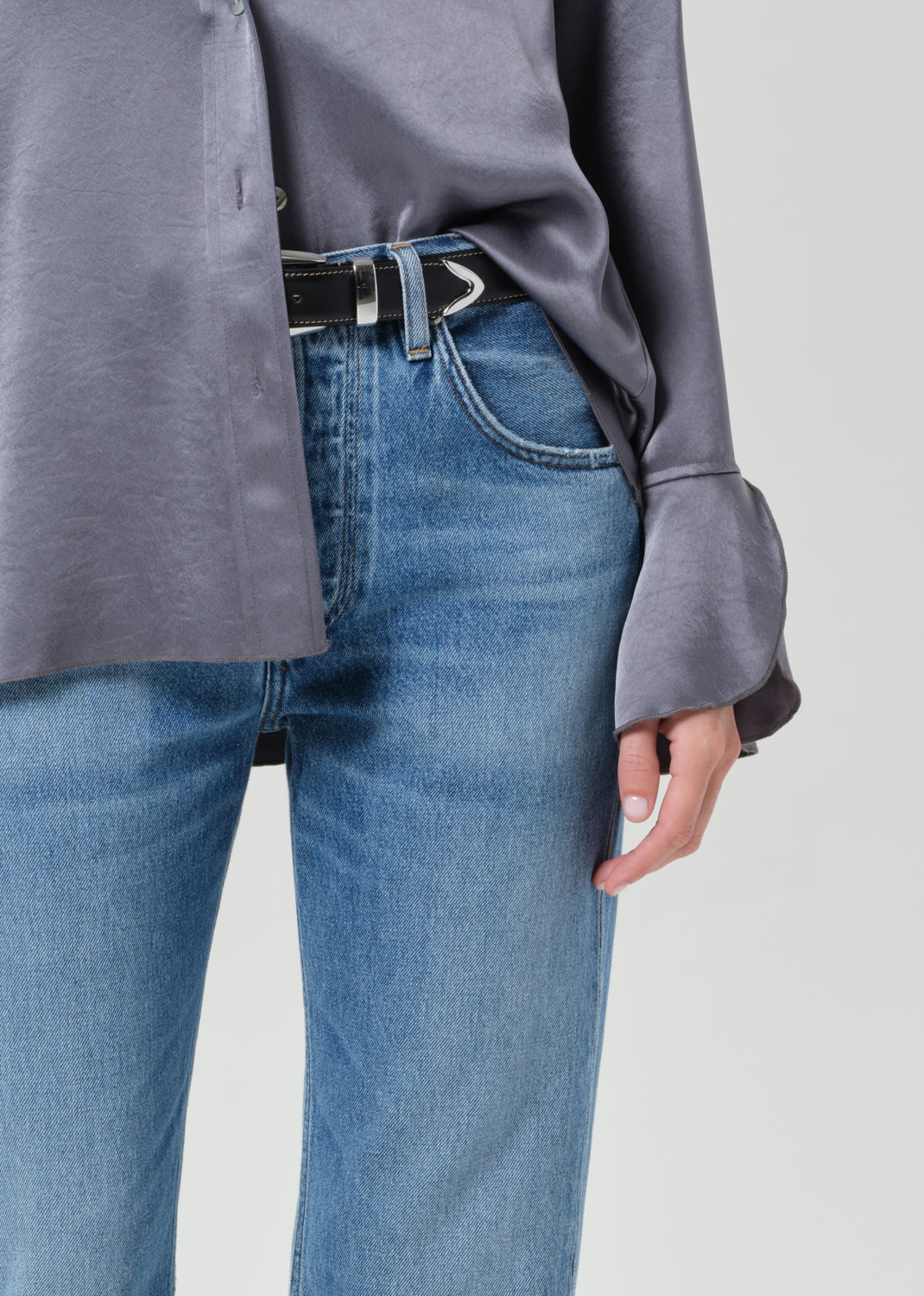 Person wearing a gray button-up shirt and blue jeans on a grey background