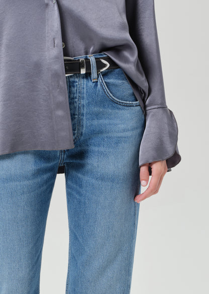 Person wearing a gray button-up shirt and blue jeans on a grey background