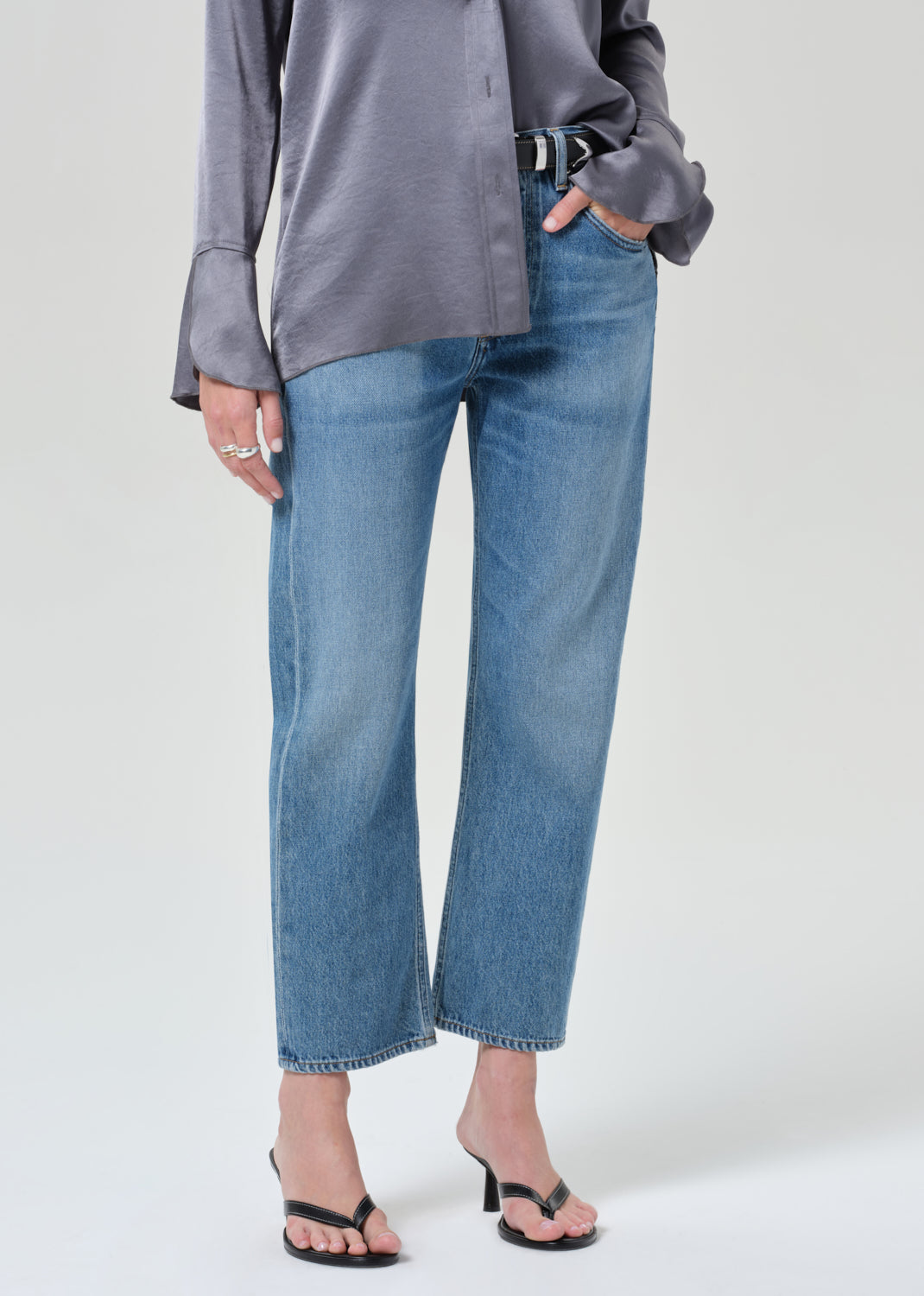 Person wearing a gray button-up shirt and blue jeans on a grey background