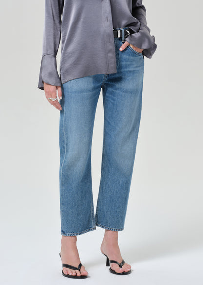 Person wearing a gray button-up shirt and blue jeans on a grey background