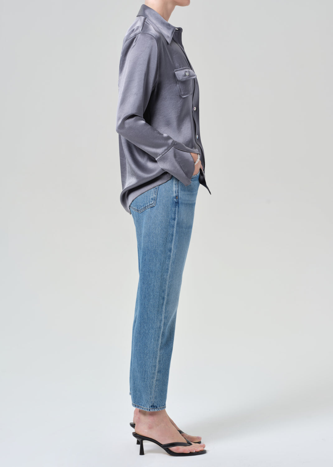 Person wearing a gray button-up shirt and blue jeans on a grey background