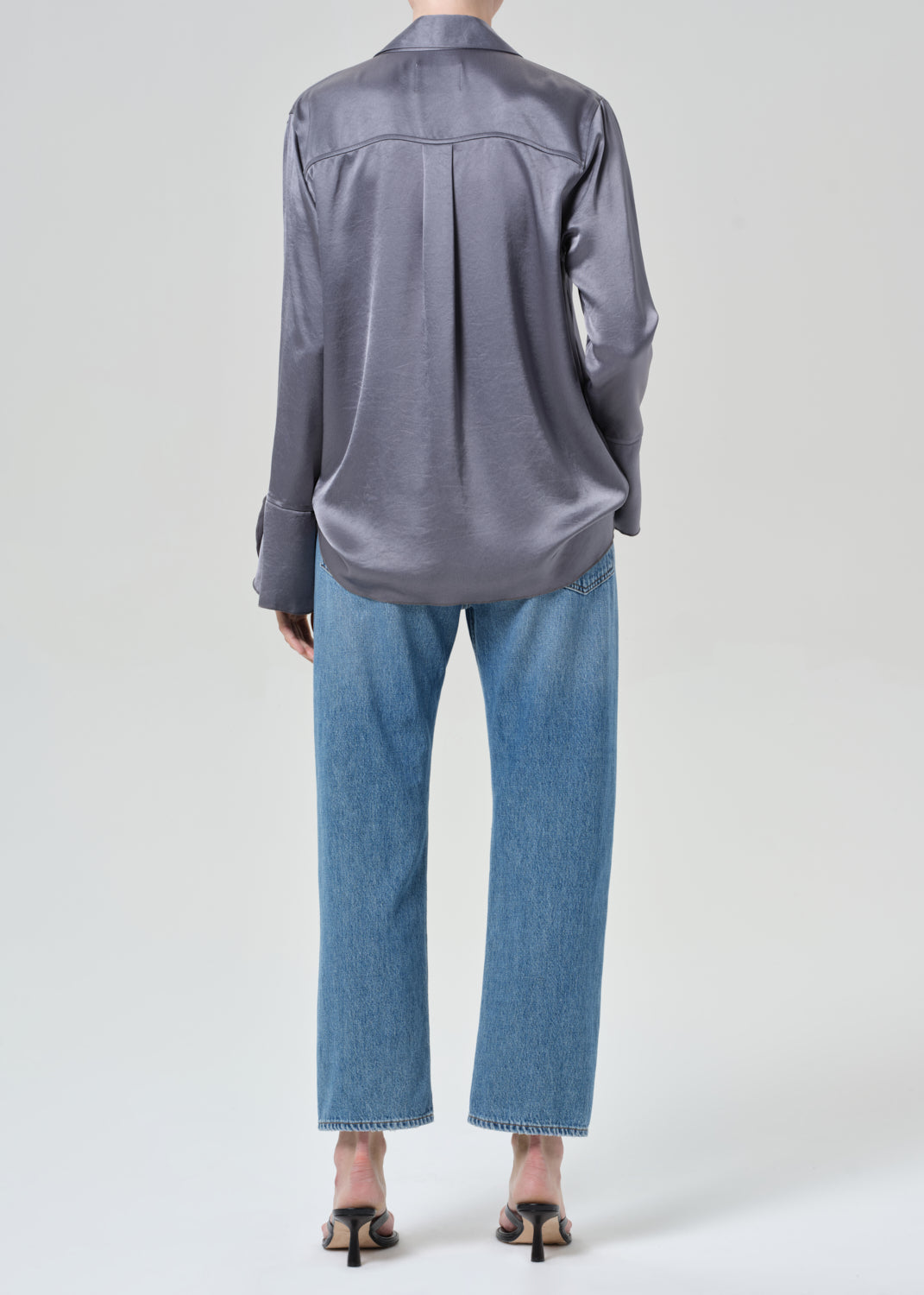 Person wearing a gray button-up shirt and blue jeans on a grey background