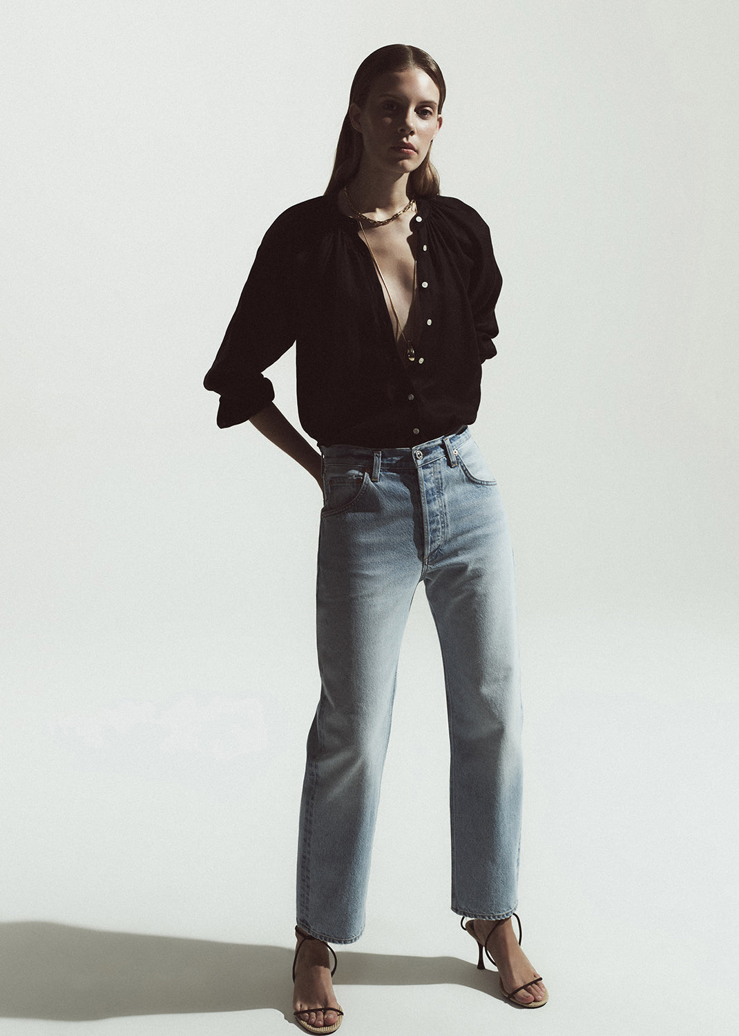Woman wearing a brown shirt and light blue jeans on a grey background