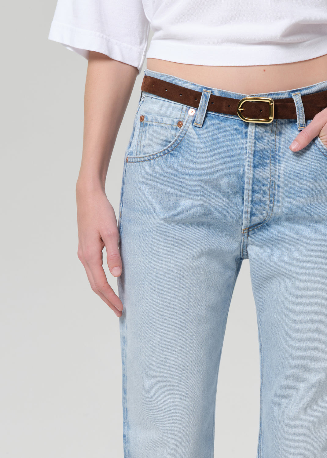 Light blue jeans with a brown belt and white top on a plain background