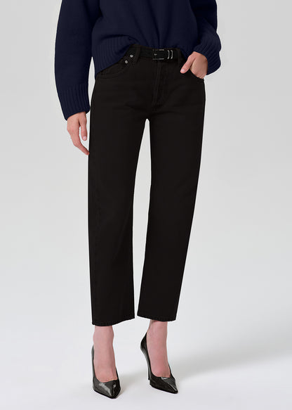 A model wearing black cropped ankle-length jeans with a straight-leg fit, styled with a navy sweater and black pointed-toe heels against a grey background.