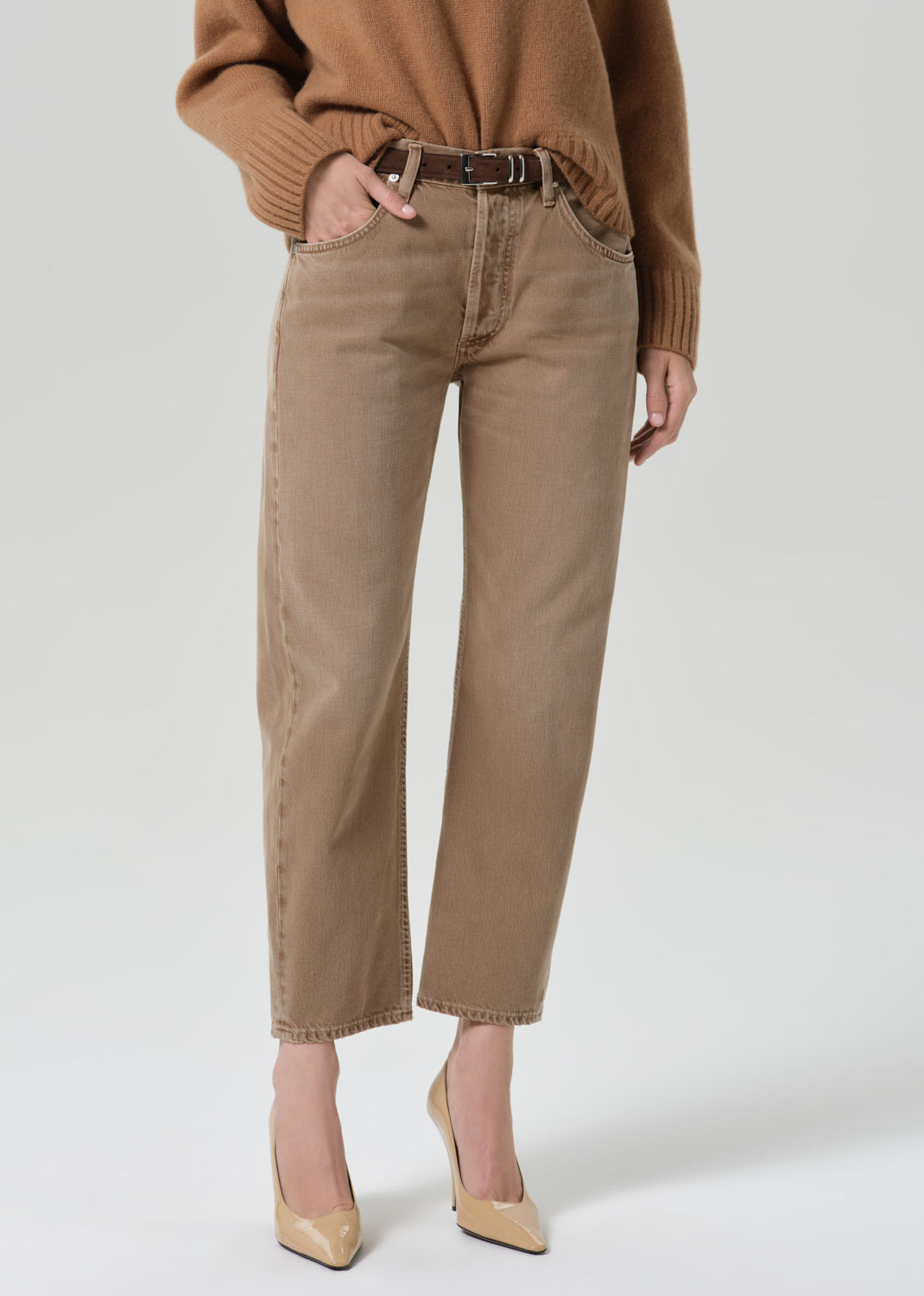 Person wearing tan straight leg pants with a brown turtleneck sweater on a grey background