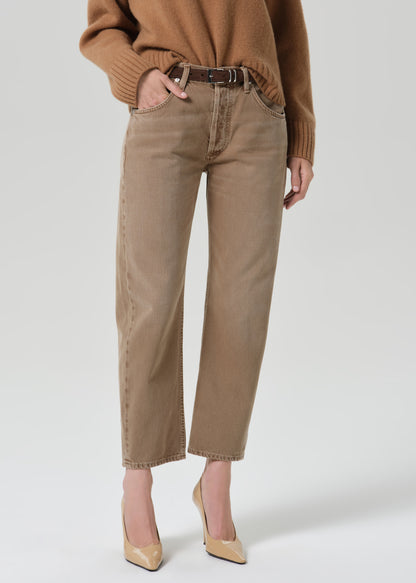 Person wearing tan straight leg pants with a brown turtleneck sweater on a grey background