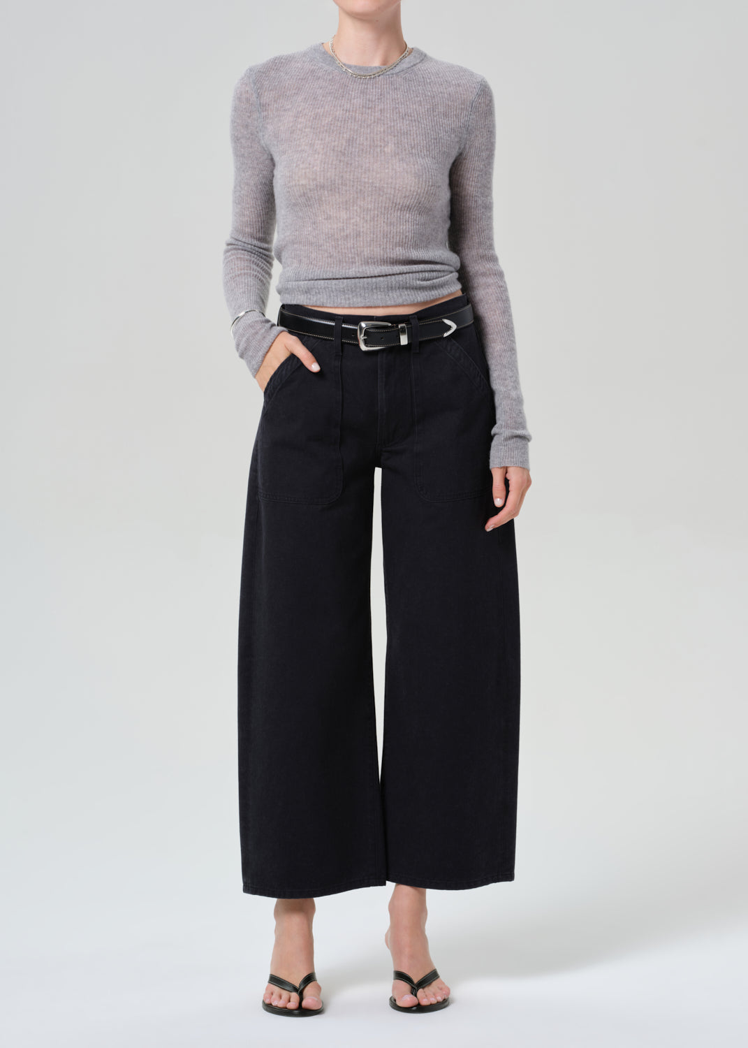 Person wearing a gray sweater and black wide-leg pants on a grey background