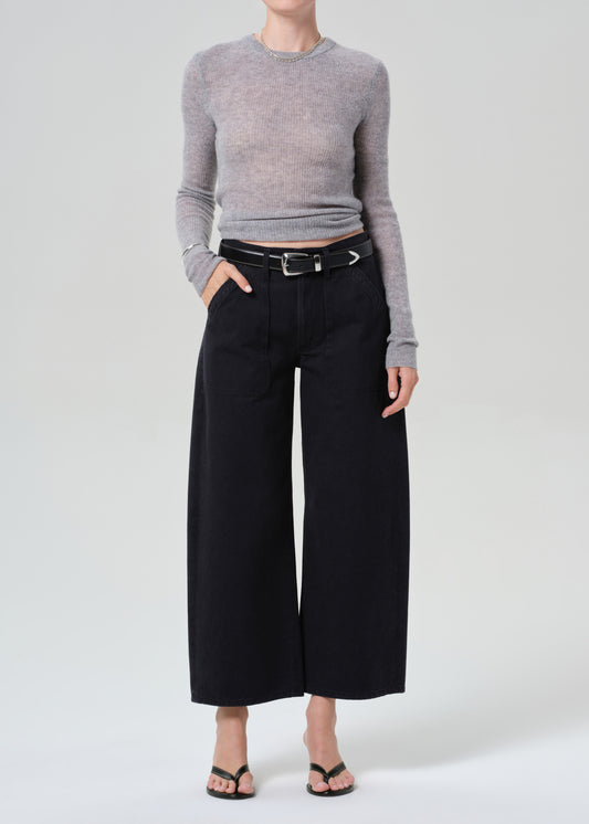 Person wearing a gray sweater and black wide-leg pants on a grey background