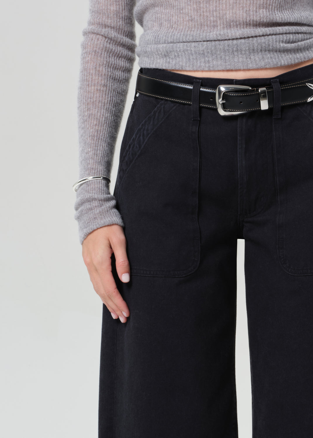 Person wearing a gray sweater and black wide-leg pants on a grey background