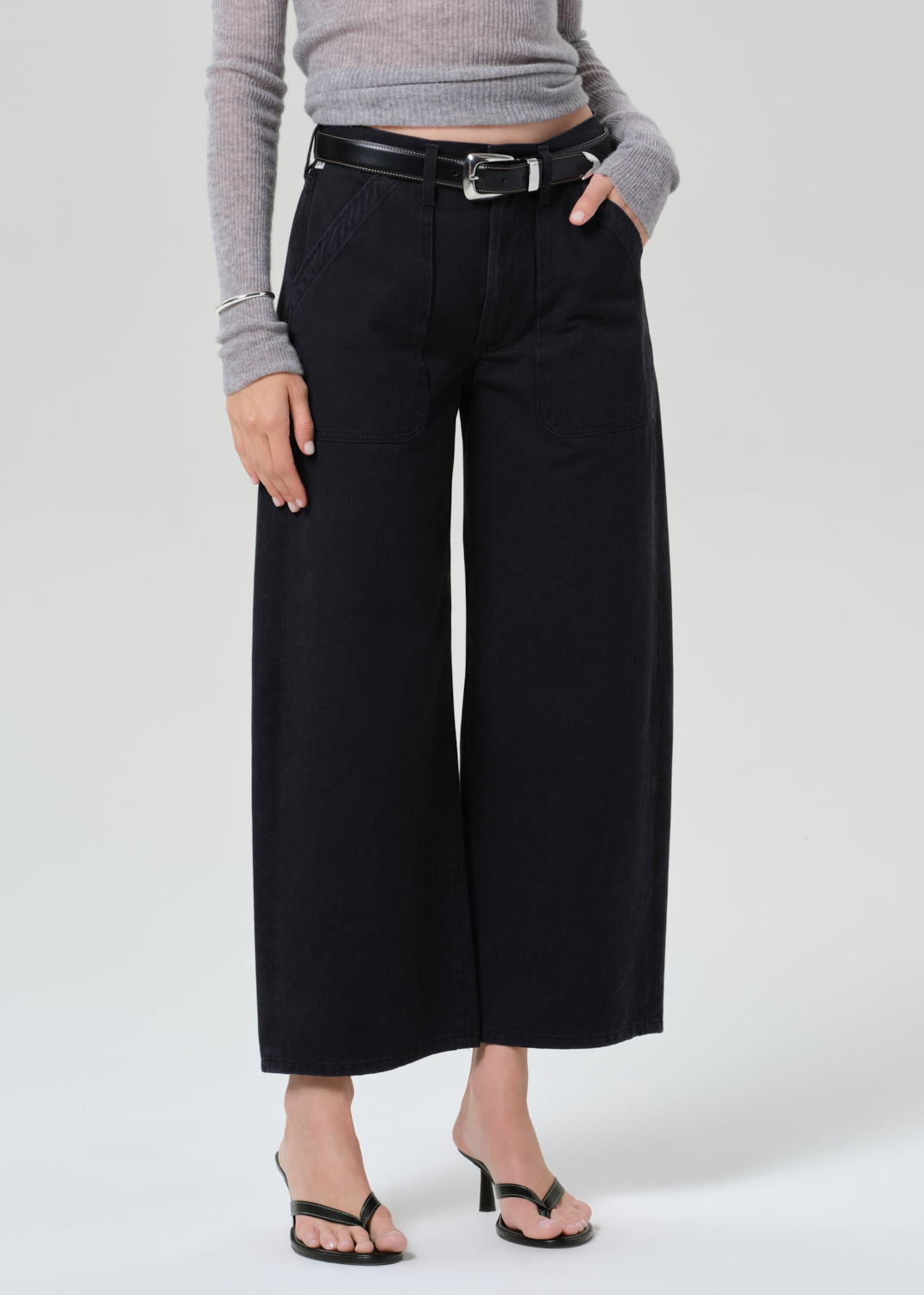 Person wearing a gray sweater and black wide-leg pants on a grey background