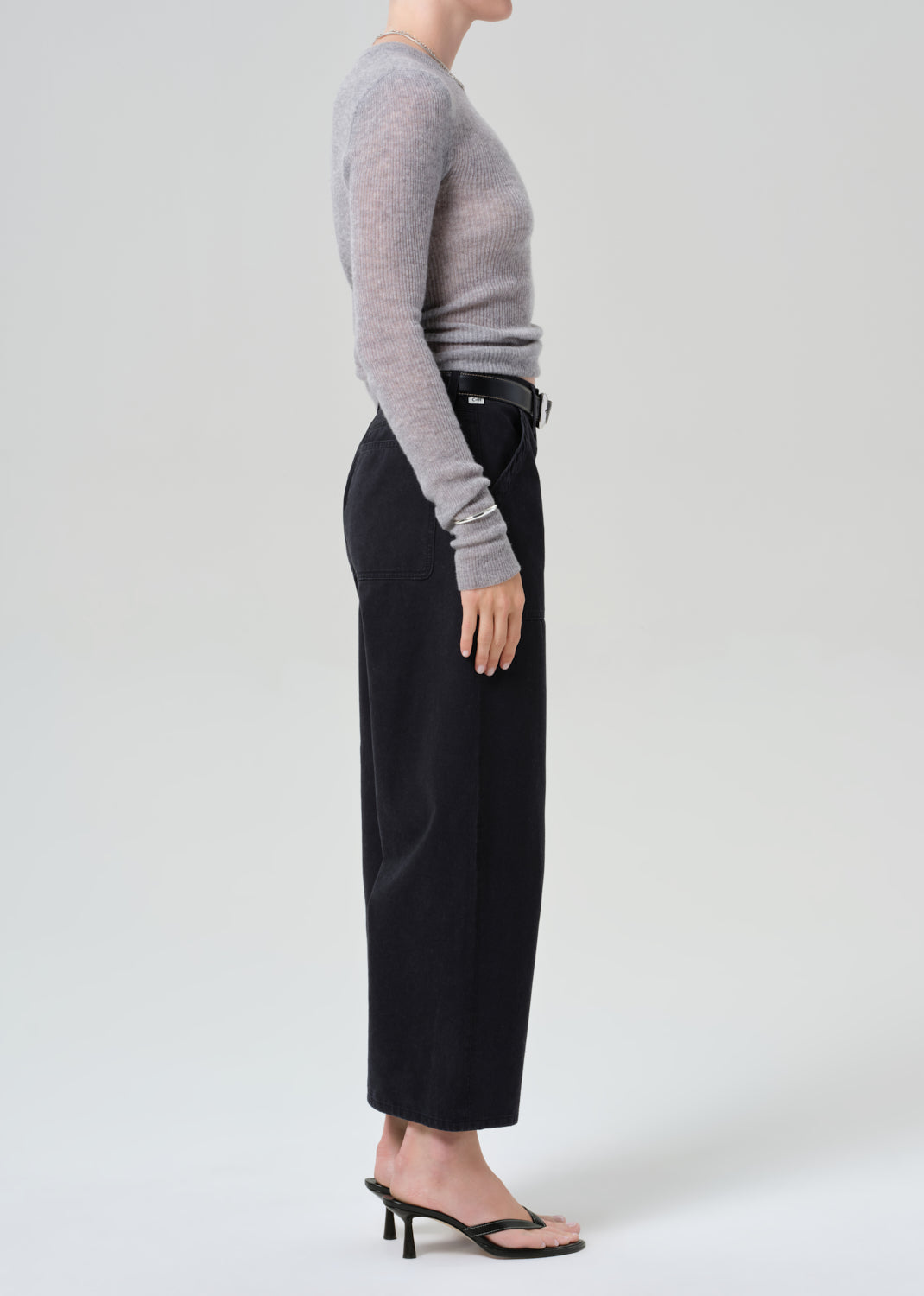 Person wearing a gray sweater and black wide-leg pants on a grey background