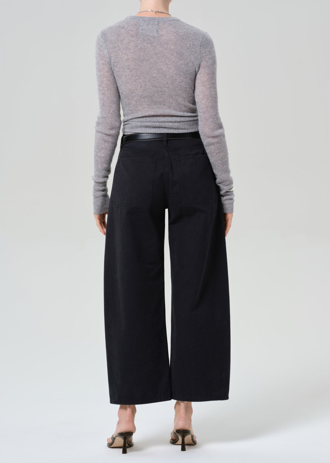 Person wearing a gray sweater and black wide-leg pants on a grey background