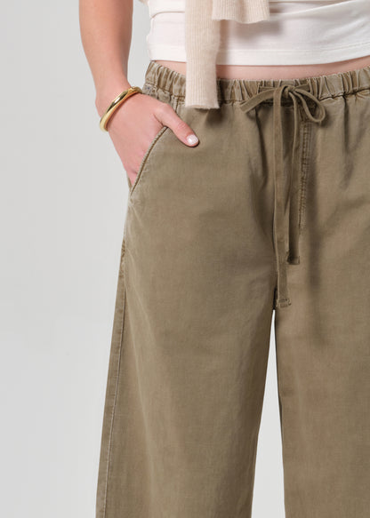 Person wearing a white t-shirt and olive brown wide-leg pants on a grey background