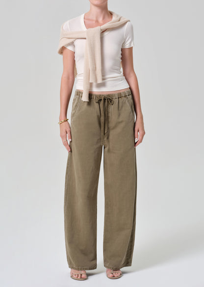 Person wearing a white top and olive brown pants with a beige sweater on a light gray background