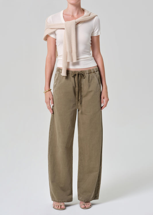 Person wearing a white top and olive brown pants with a beige sweater on a light gray background