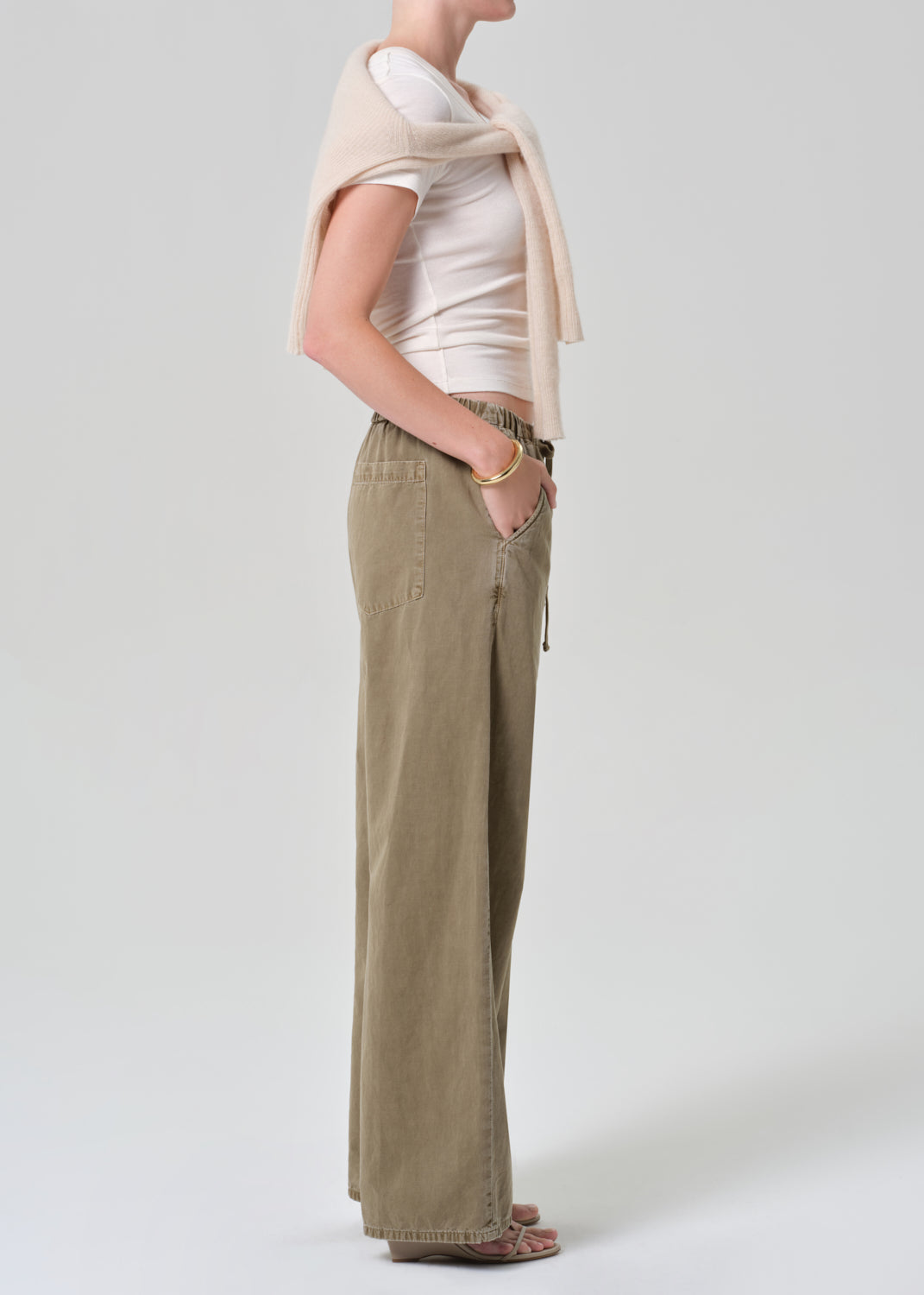 Person wearing a white t-shirt and olive brown wide-leg pants on a grey background