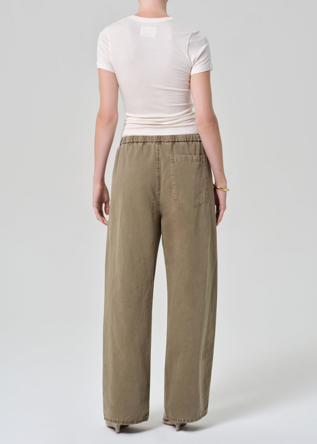 Person wearing a white t-shirt and olive brown wide-leg pants on a grey background