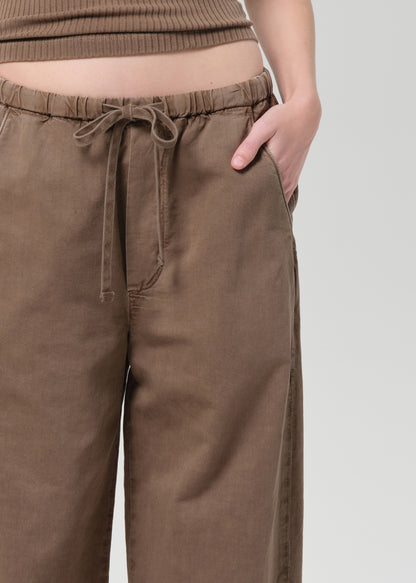 Person wearing a brown ribbed tank top and wide-leg pants on a plain background