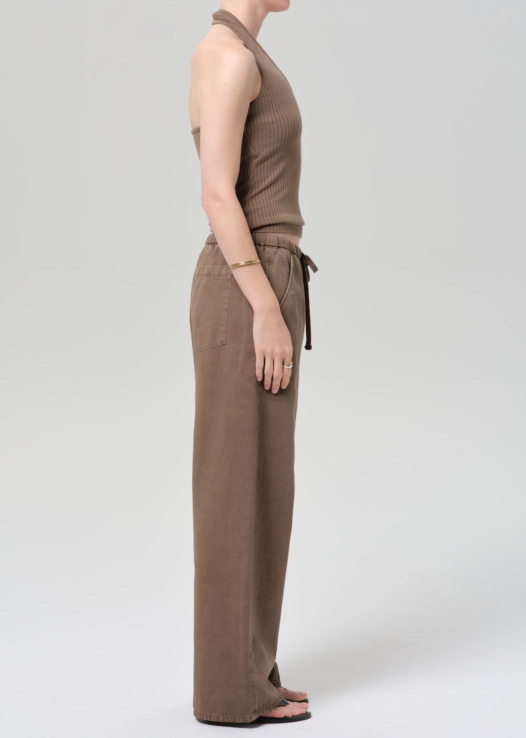 Person wearing a brown ribbed tank top and wide-leg pants on a plain background
