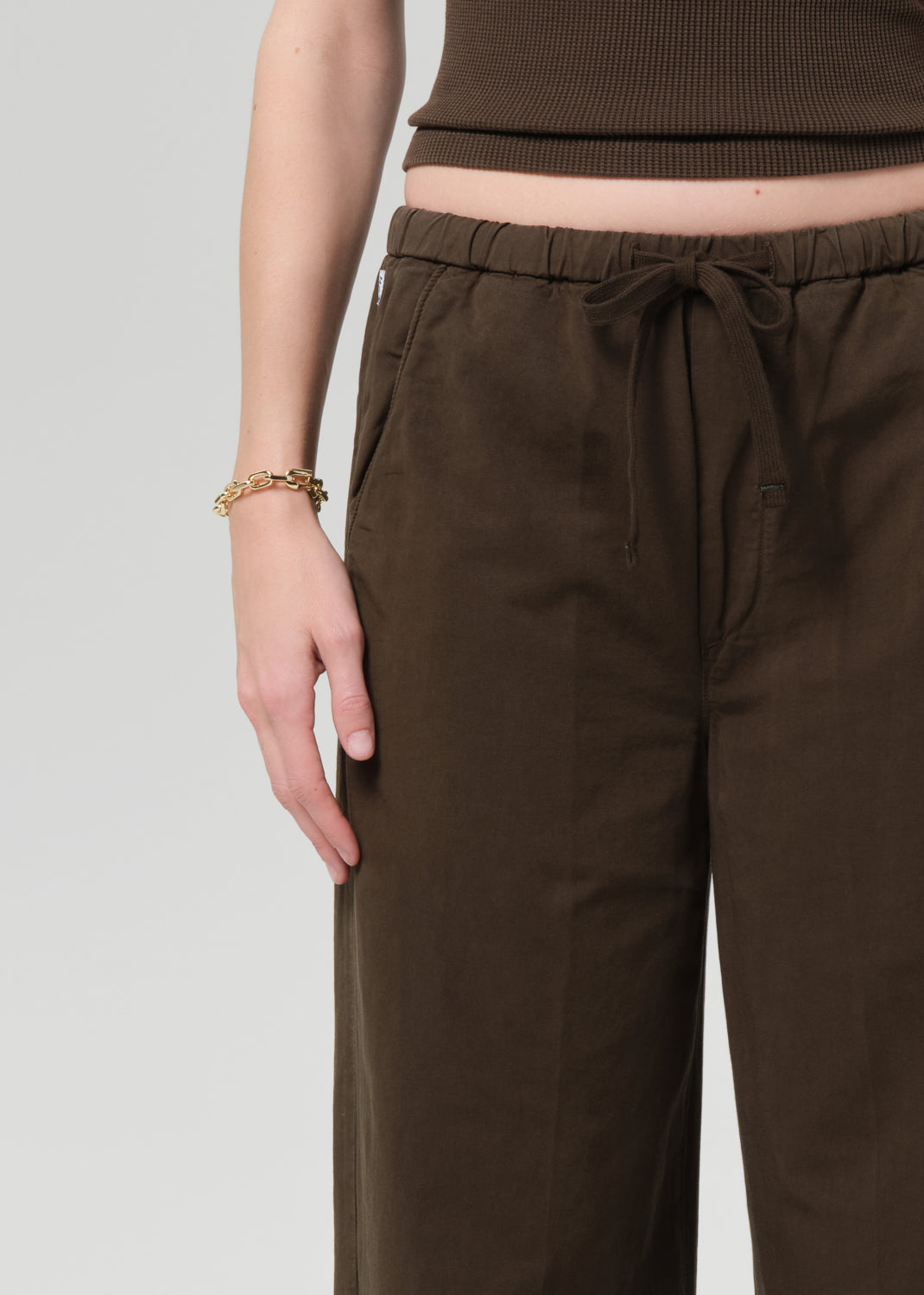 Person wearing a brown outfit with a top and wide-leg pants on a grey background