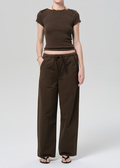 Person wearing a brown outfit with a top and wide-leg pants on a grey background
