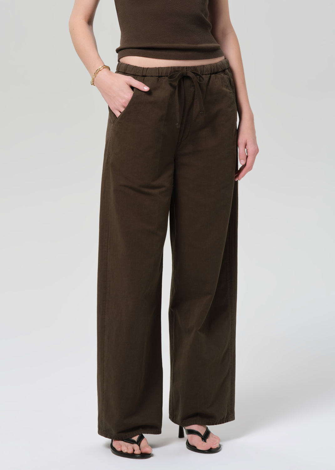 Person wearing a brown outfit with a top and wide-leg pants on a grey background
