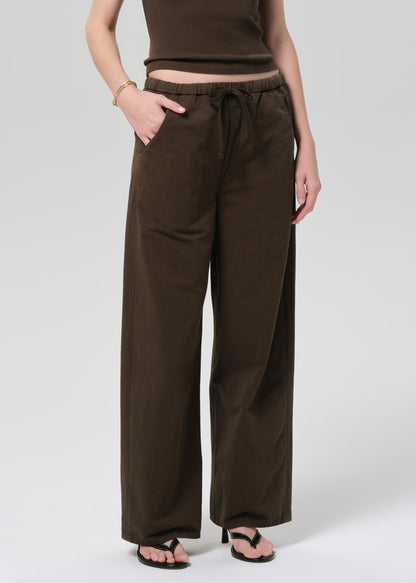 Person wearing a brown outfit with a top and wide-leg pants on a grey background