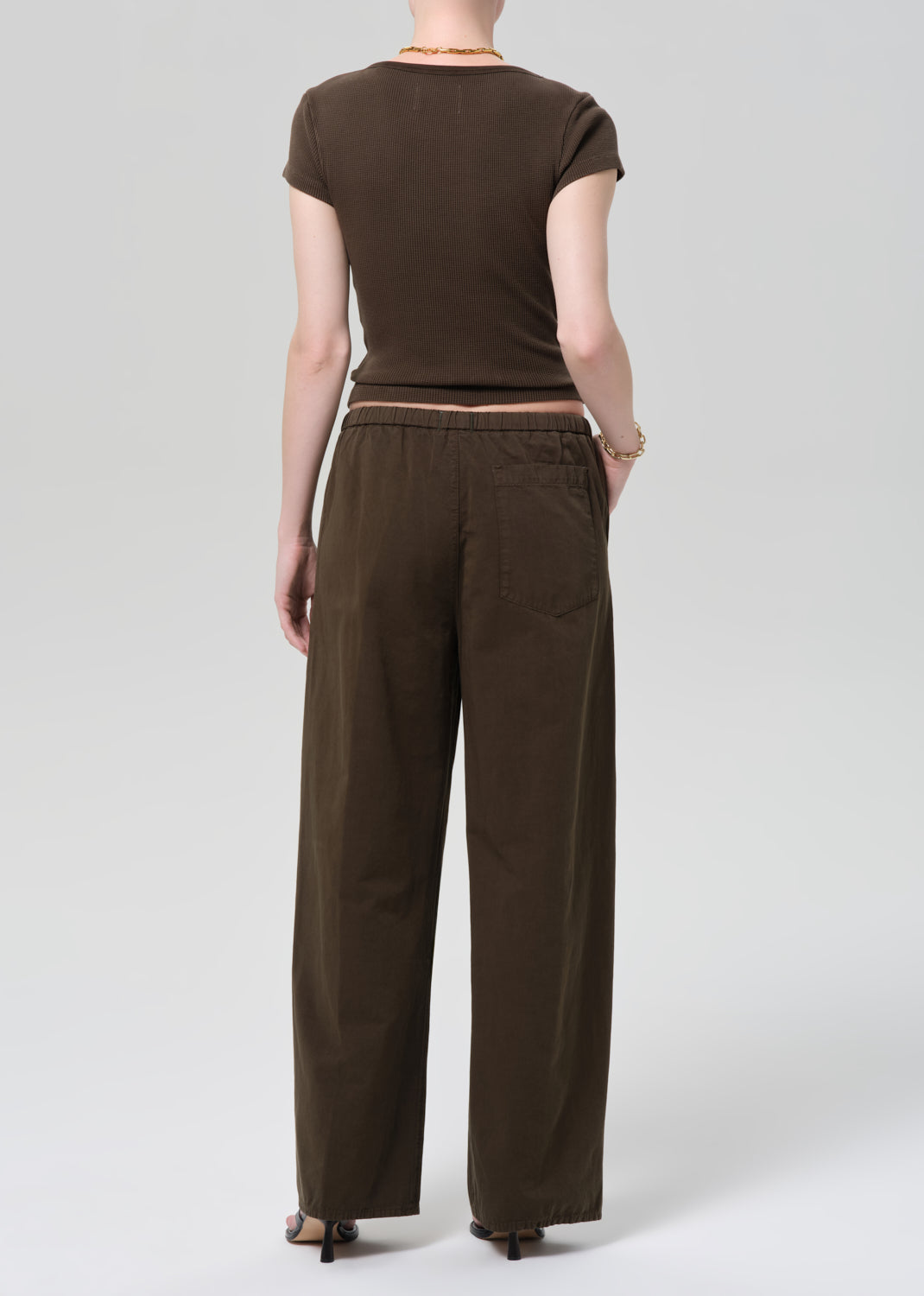 Person wearing a brown outfit with a top and wide-leg pants on a grey background