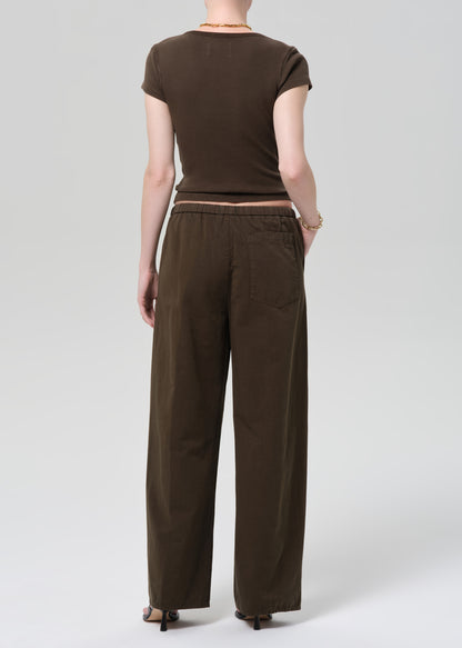 Person wearing a brown outfit with a top and wide-leg pants on a grey background