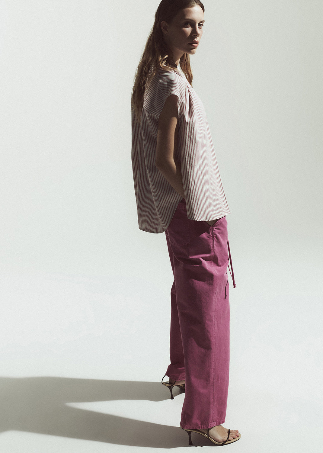 Woman wearing a light-colored top and magenta pants against a plain background