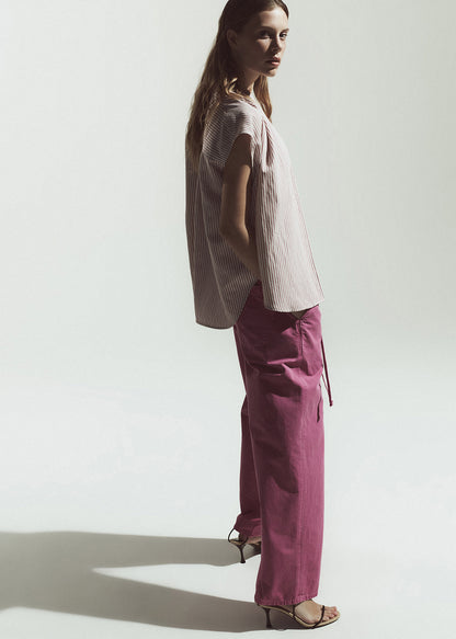 Woman wearing a light-colored top and magenta pants against a plain background