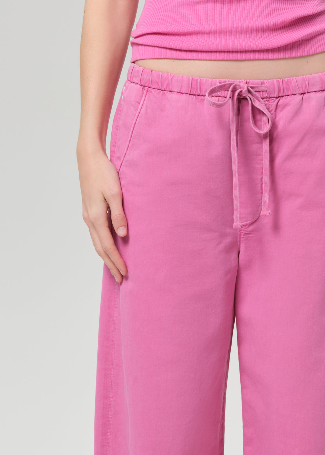 Person wearing a pink sleeveless top and wide-leg pants on a plain background