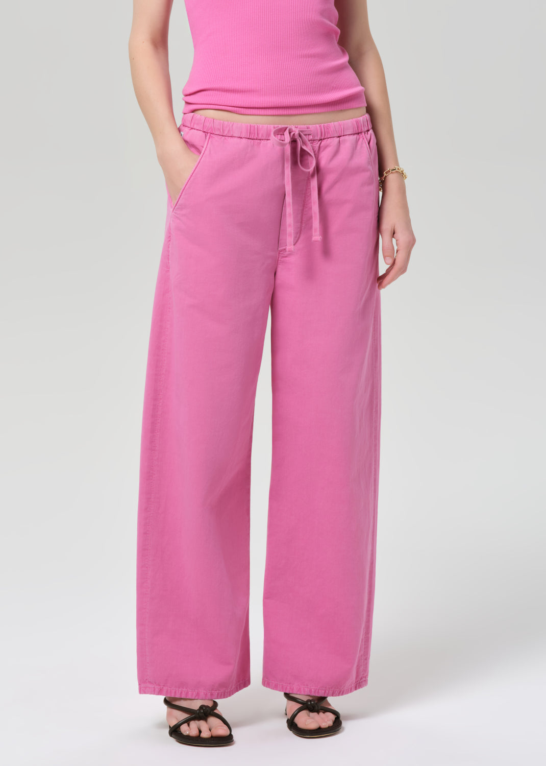 Person wearing a pink sleeveless top and wide-leg pants on a plain background