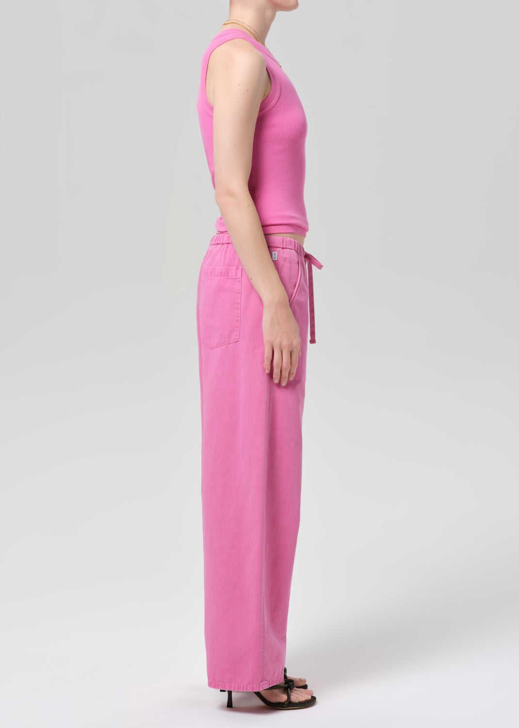 Person wearing a pink sleeveless top and wide-leg pants on a plain background